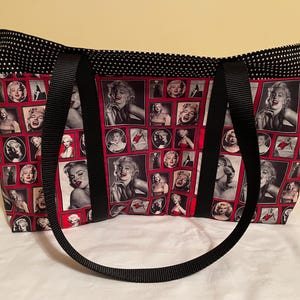 May include: A tote bag featuring a collage of black and white images of Marilyn Monroe on a red background. The bag has black handles and a black and white polka dot trim.