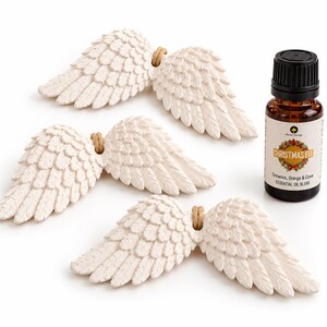 May include: Three off-white, textured angel wing ornaments with small jute loops for hanging, accompanied by a small amber glass bottle of essential oil labelled Christmas Eve with notes of cinnamon, orange, and clove.