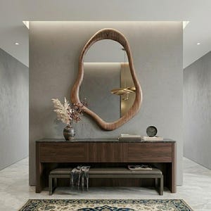 Peut inclure: Une entrée moderne avec un grand miroir en bois de forme organique. En dessous, une console en bois foncé avec des tiroirs et un banc. Un vase de fleurs séchées et une petite horloge ajoutent des touches décoratives. L'espace est éclairé par un éclairage encastré.