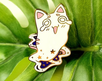 Puede incluir: Un pin de esmalte blanco con un gato de dibujos animados que lleva una capa estrellada azul y blanca. El gato tiene orejas rosas y una lengua rosa que sobresale. El pin tiene un acabado dorado.
