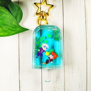 May include: A blue and green popsicle keychain with two cartoon figures inside. The keychain is attached to a gold star-shaped charm.