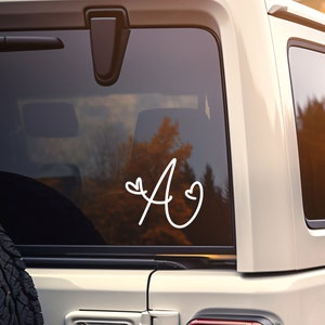 May include: A white car with a white vinyl decal of the letter "A" with two hearts on the back window.