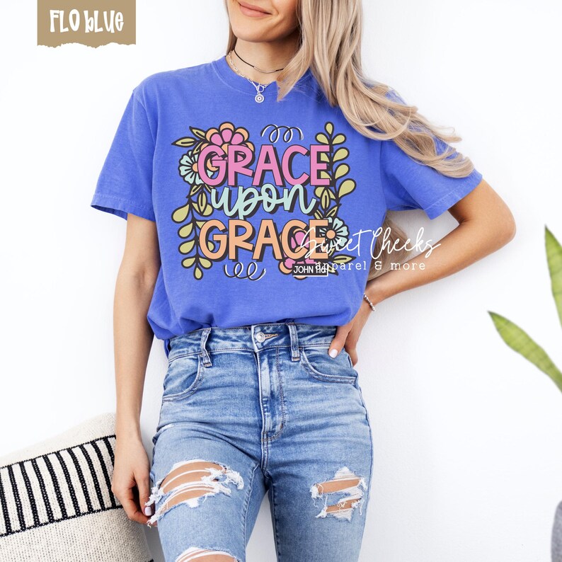 May include: A blue t-shirt with the words "GRACE upon GRACE" in a floral design. The shirt is worn with blue jeans. The text "Sweet Cheeks Apparel & more" is also visible.