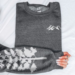 May include: A dark gray sweatshirt with a white mountain range design on the front and a white tree design on the sleeve.