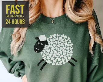 May include: A green sweatshirt with a black and white sheep graphic. The sheep is made up of white hearts.