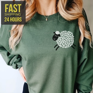 May include: A green sweatshirt with a black and white sheep graphic. The sheep is made up of white hearts.