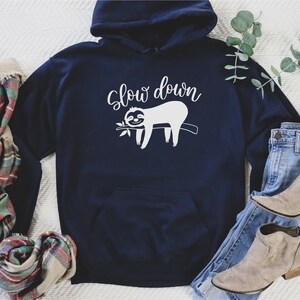 May include: A navy blue hoodie with a white graphic of a sloth hanging on a branch with the text "Slow down".