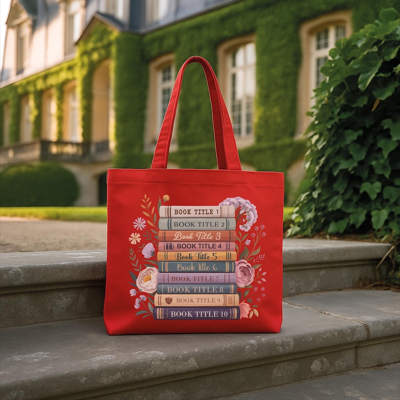 A red tote bag with a stack of colorful books printed on it, placed on a stone step in front of a building with ivy.