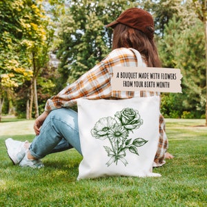 K&ouml;nnte beinhalten: Eine wei&szlig;e Einkaufstasche mit einem gr&uuml;nen Blumenmuster. Die Tasche tr&auml;gt den Text "Ein Strau&szlig; aus Blumen deines Geburtsmonats".