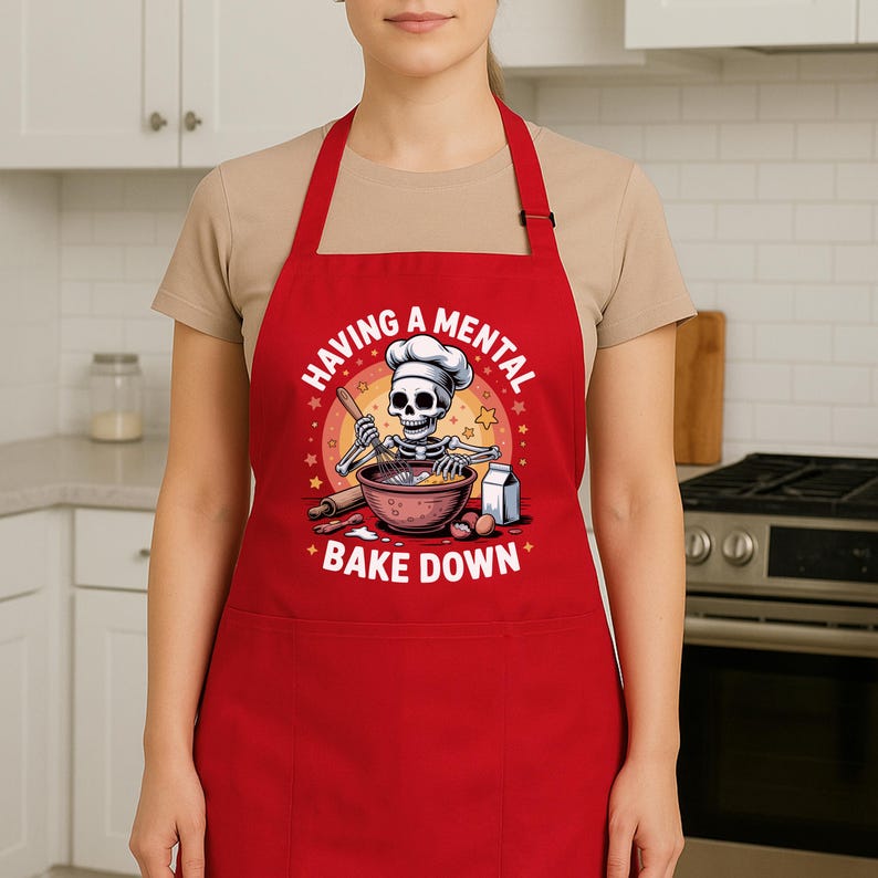 May include: A red apron featuring the phrase "HAVING A MENTAL BAKE DOWN" and a cartoon skeleton chef. The skeleton is wearing a chef's hat and mixing ingredients in a bowl. The apron has a front pocket and neck strap.
