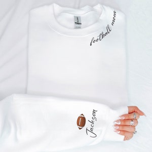 May include: White sweatshirt with the text "football mom" on the front and a football graphic and the text "Jackson" on the sleeve.