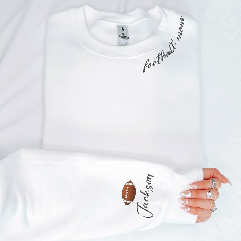 May include: White sweatshirt with the text "football mom" on the front and a football graphic and the text "Jackson" on the sleeve.