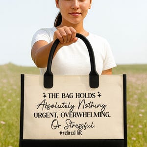 A woman holding a large tote bag with text on it, standing in a field with a clear blue sky in the background.