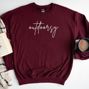 May include: A maroon sweatshirt with the word "outdoorsy" written in white script on the front.