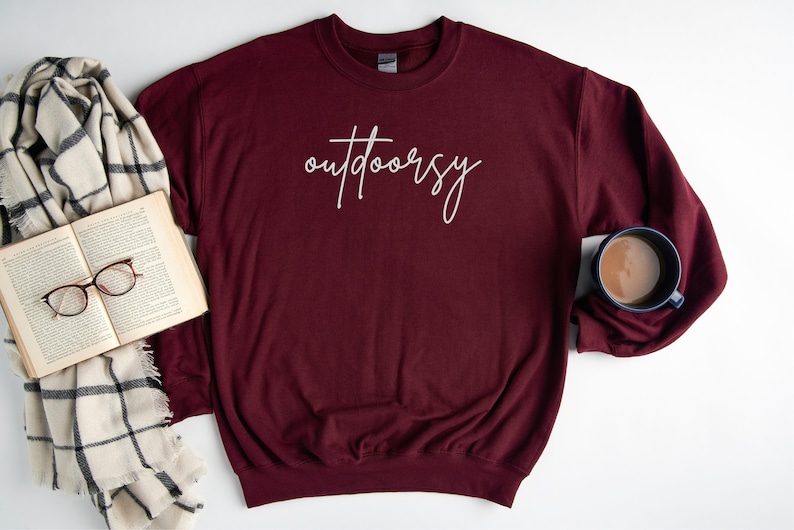 May include: A maroon sweatshirt with the word "outdoorsy" written in white script on the front.