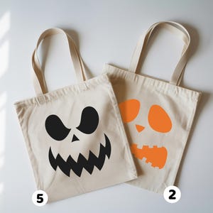 two tote bags with Halloween-themed designs, including a white bag with a black jack-o-lantern face and an orange bag with a similar face.