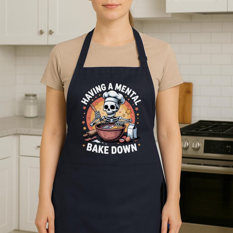 May include: A dark blue apron featuring a cartoon skeleton chef baking, with the words "HAVING A MENTAL BAKE DOWN" encircling the image. The skeleton wears a chef's hat and is stirring a bowl.