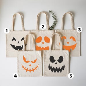 a collection of five tote bags with Halloween-themed designs, including jack-o-lantern faces and other spooky patterns.