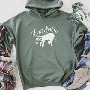 May include: A green hooded sweatshirt with a white graphic of a sloth on a branch and the text "Slow down".