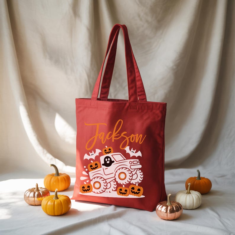 A red tote bag with a Halloween-themed design, including a monster truck and jack-o-lanterns, is displayed against a white background.