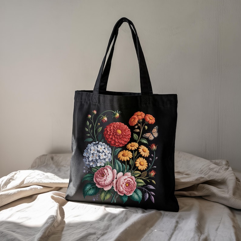 May include: Black tote bag with a colourful floral print. The design showcases a red dahlia, pink roses, yellow daisies, and a butterfly. The bag has two black handles and is made of a durable fabric, ideal for shopping or carrying items.