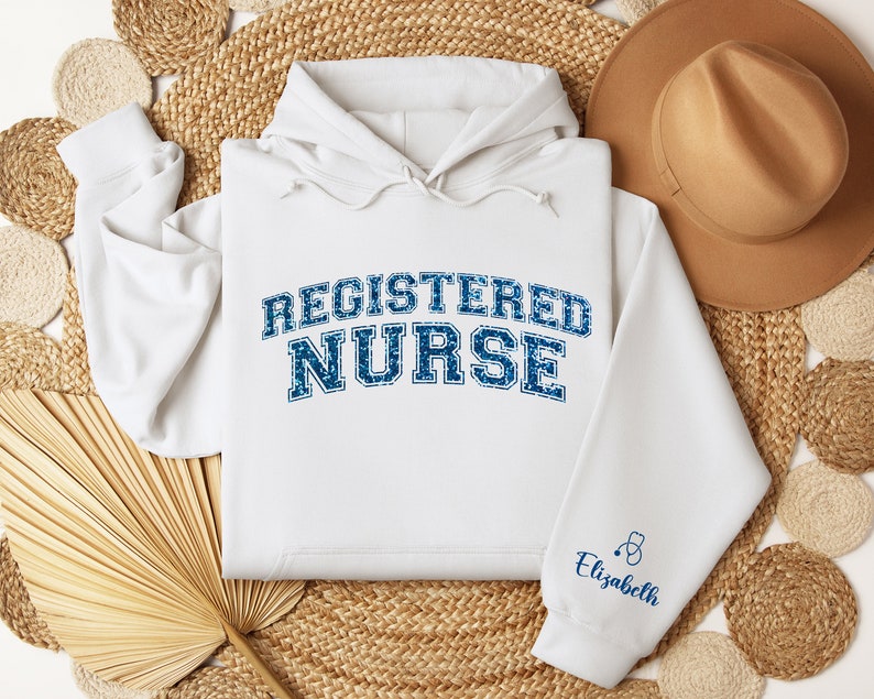 May include: White hoodie with the text "REGISTERED NURSE" in blue with a distressed look. The sleeve has a small blue stethoscope and the name "Elizabeth" in blue text.