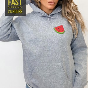 Op de afbeelding: Een grijs gem&ecirc;leerd hoodie met een klein watermeloen motief op de voorkant. De hoodie heeft een kangoeroezak en een capuchon met trekkoord.