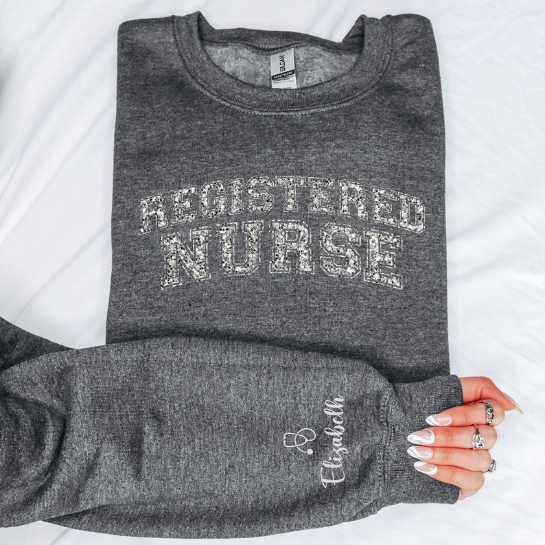 May include: Gray sweatshirt with the text "REGISTERED NURSE" in silver glitter. The sweatshirt has a small embroidered stethoscope and the name "Elizabeth" on the sleeve.