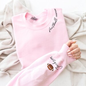 May include: Pink sweatshirt with the text "football mom" on the shoulder and "Jackson" with a football graphic on the sleeve.