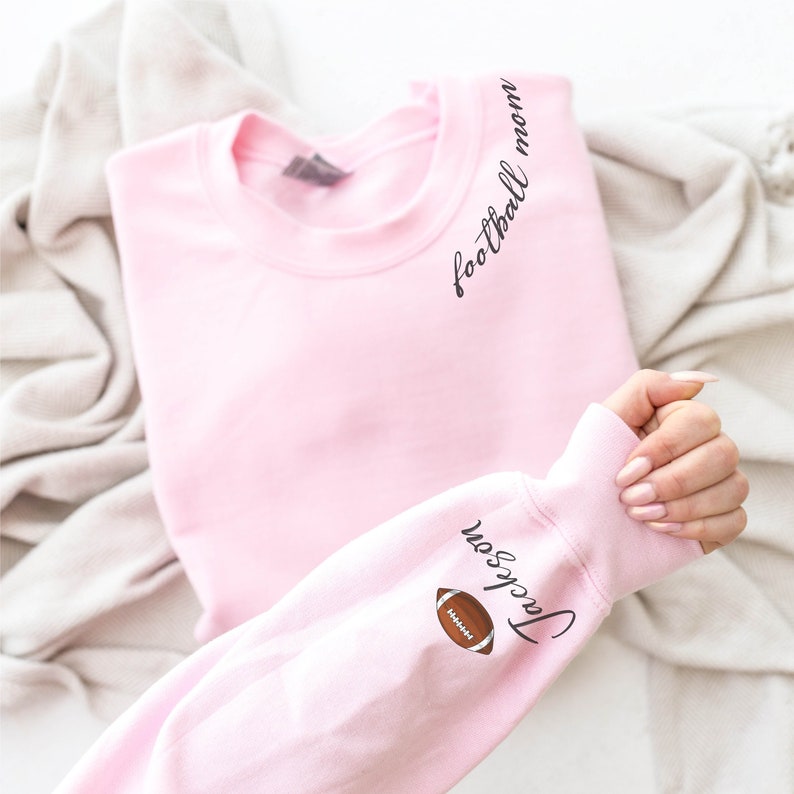 May include: Pink sweatshirt with the text "football mom" on the shoulder and "Jackson" with a football graphic on the sleeve.