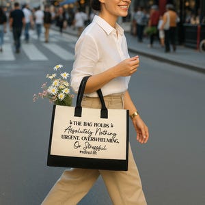 A woman wearing sunglasses and carrying a bag with text printed on it is walking down a city street.