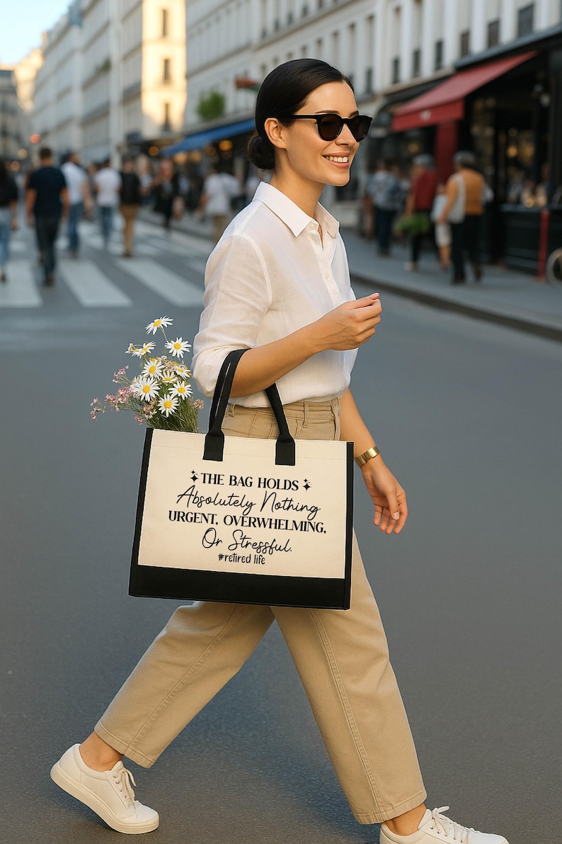 A woman wearing sunglasses and carrying a bag with text printed on it is walking down a city street.