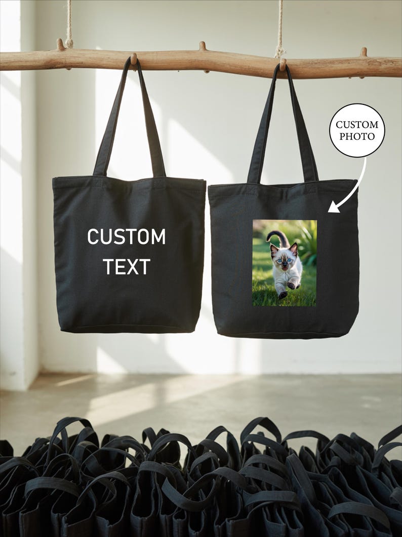 two black tote bags hanging from a wooden bar, with one bag having a custom photo printed on it.