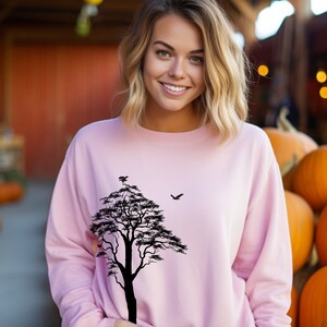 May include: A pink sweatshirt with a black silhouette of a tree and a bird on the front.
