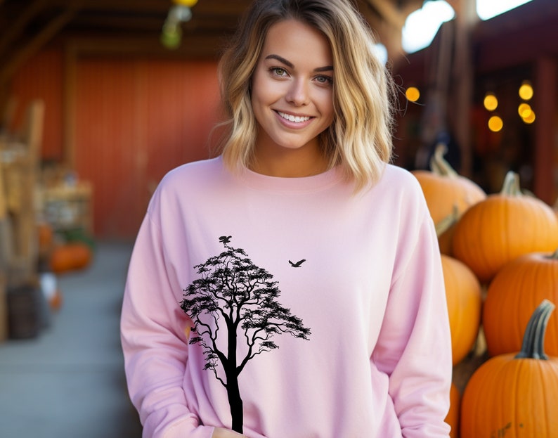 May include: A pink sweatshirt with a black silhouette of a tree and a bird on the front.
