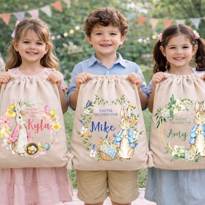 May include: Three children holding beige drawstring bags with Easter-themed designs. Each bag features a bunny illustration, floral wreath, and the text "Easter Delivery For" followed by a name. The bags are filled with gifts.