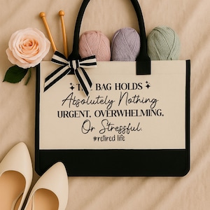 A handbag with a humorous quote printed on it, accompanied by knitting needles, yarn balls, and a pair of white shoes.