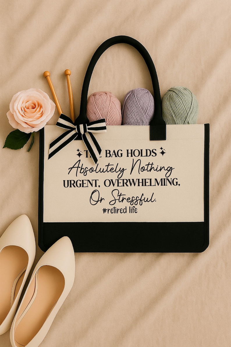 A handbag with a humorous quote printed on it, accompanied by knitting needles, yarn balls, and a pair of white shoes.