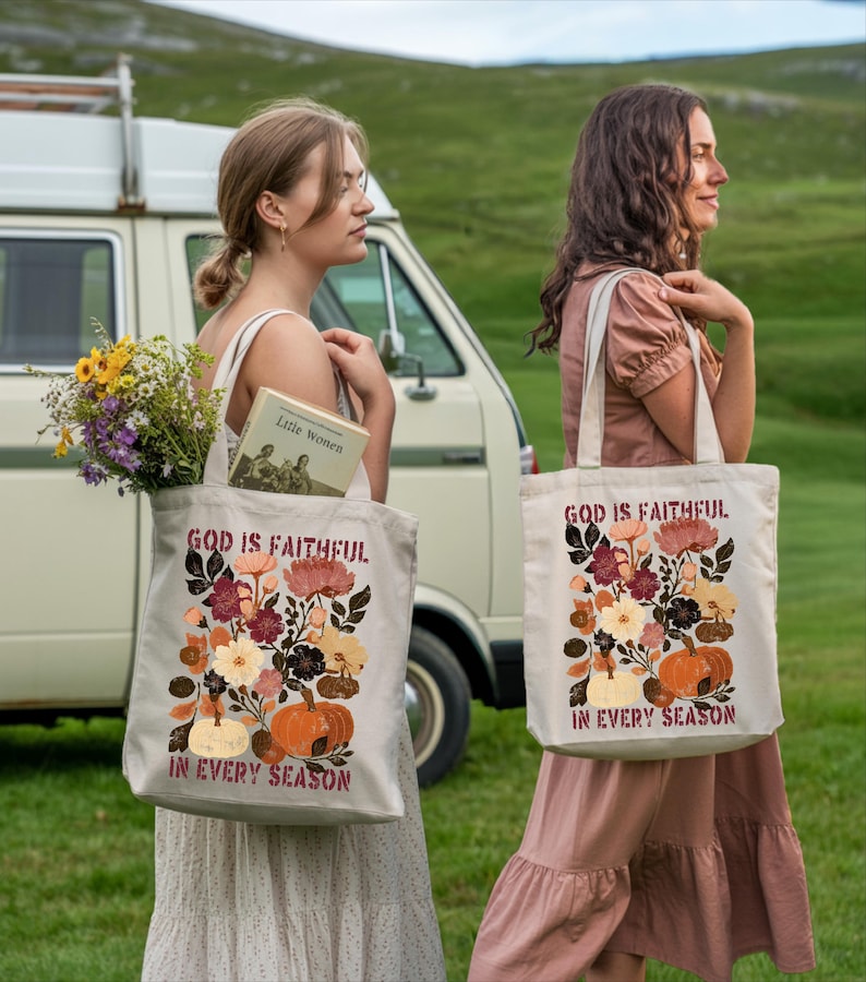 Two women standing in a grassy field, each carrying a tote bag with a floral design and text.