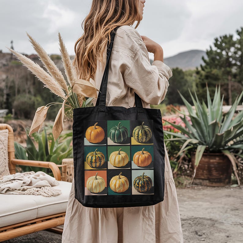 Pu&ograve; includere: Borsa tote nera con una griglia di nove illustrazioni di zucche colorate. Ogni zucca &egrave; ambientata su un quadrato di colore diverso, tra cui arancione, verde e giallo. La borsa ha due manici neri.