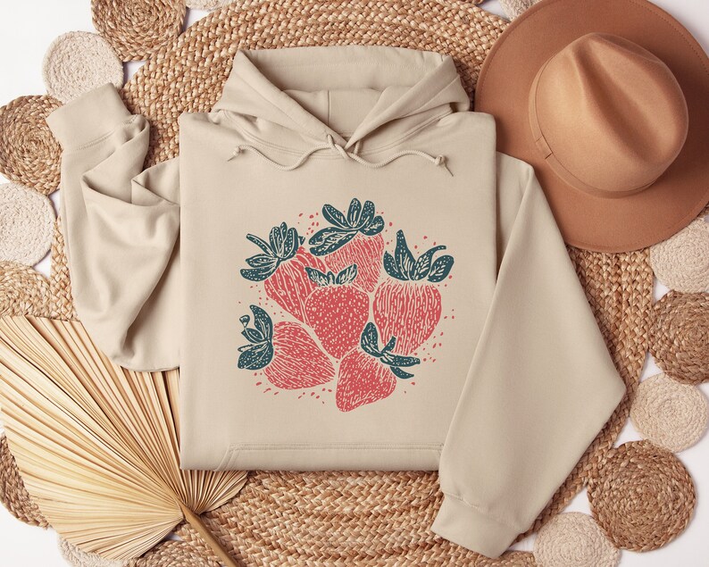 May include: A beige hoodie with a graphic print of red strawberries with green leaves on the front.