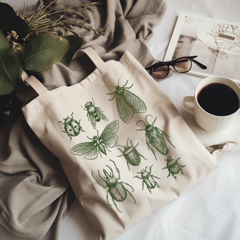 May include: A beige canvas tote bag featuring green insect illustrations. The insects include a beetle, a moth, a dragonfly, a cockroach, and a stag beetle.