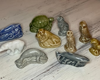 May include: A collection of nine ceramic figurines depicting various animals, including a turtle, owl, monkey, polar bear, seal, and a bird. The figurines are painted in various colors, including green, brown, white, and gray.
