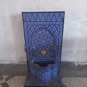 Puede incluir: Una fuente de azulejos azules y blancos con un dise&ntilde;o decorativo. La fuente tiene una peque&ntilde;a cuenca y un ca&ntilde;o. Est&aacute; sobre ruedas y est&aacute; lista para ser utilizada.