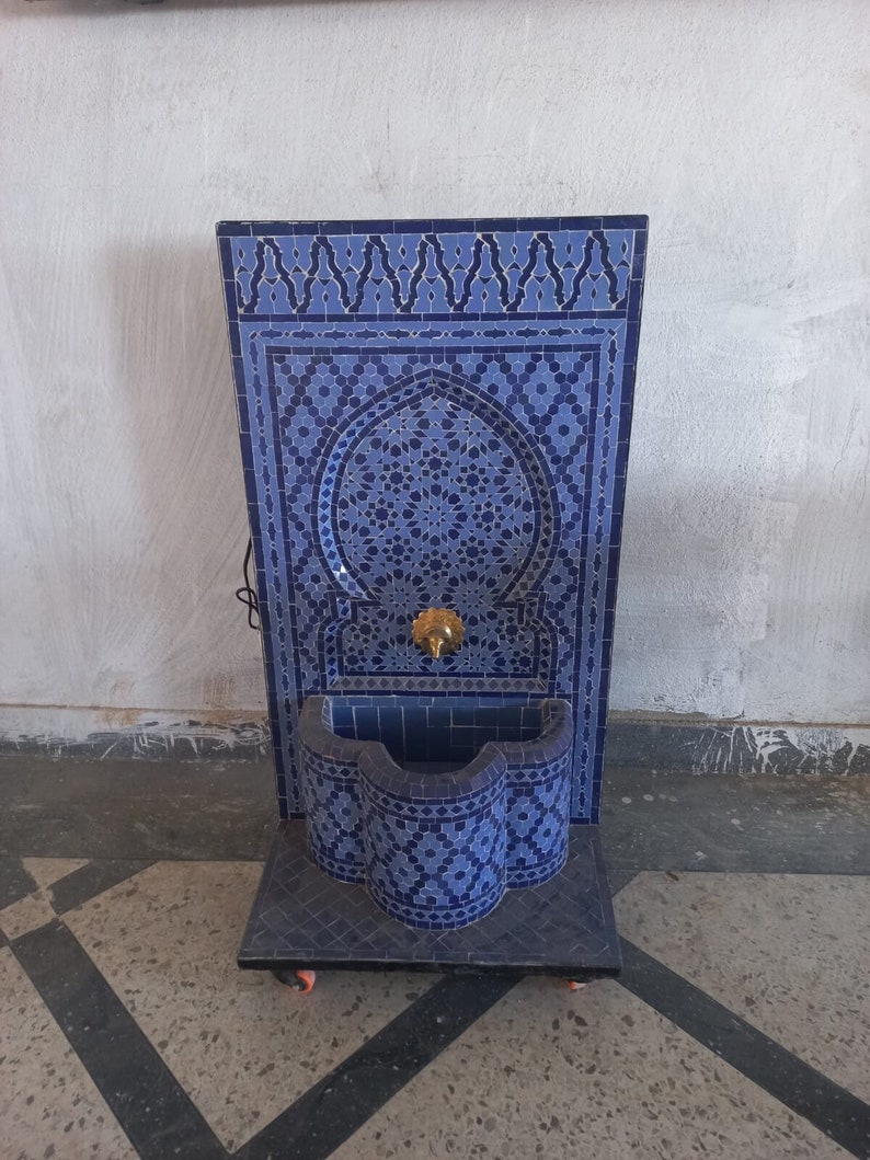 Puede incluir: Una fuente de azulejos azules y blancos con un dise&ntilde;o decorativo. La fuente tiene una peque&ntilde;a cuenca y un ca&ntilde;o. Est&aacute; sobre ruedas y est&aacute; lista para ser utilizada.