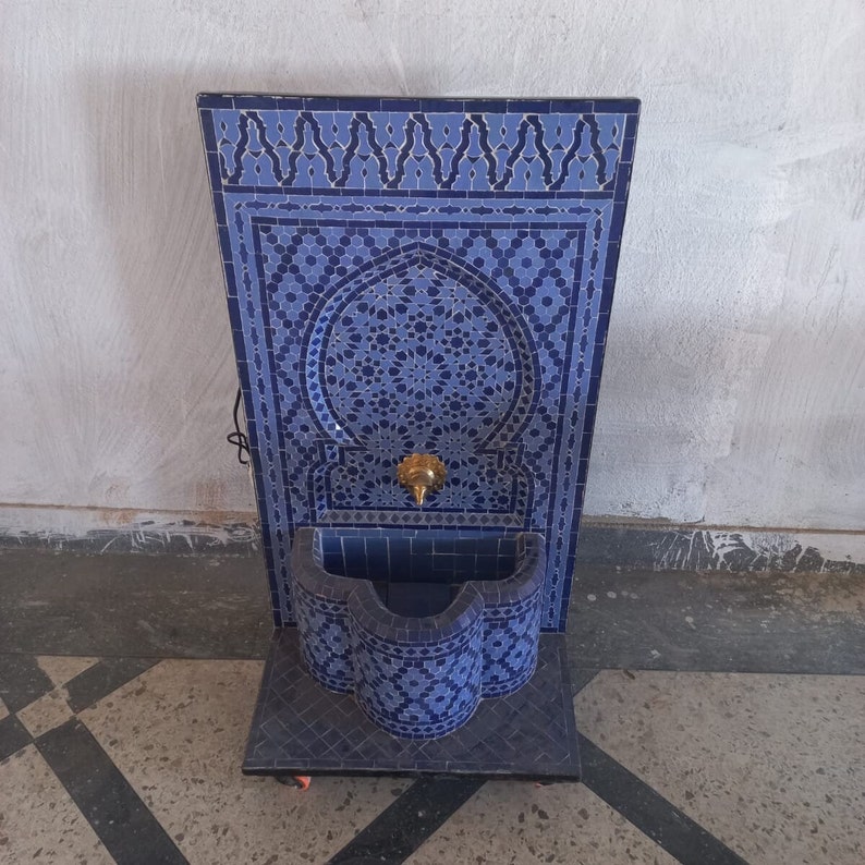 Puede incluir: Una fuente de azulejos azules y blancos con un arco decorativo y una peque&ntilde;a cuenca. La fuente est&aacute; montada en un soporte con ruedas.