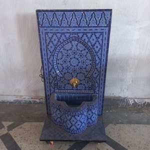 Puede incluir: Una fuente de azulejos azules y blancos con un arco decorativo y un ca&ntilde;o de lat&oacute;n. La fuente est&aacute; montada en un soporte con ruedas.