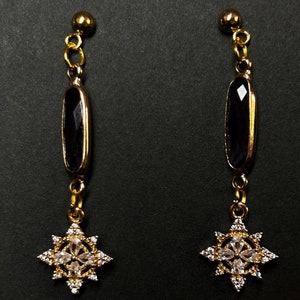 May include: A pair of gold earrings with a dark purple oval-shaped stone and a star-shaped design with clear rhinestones.