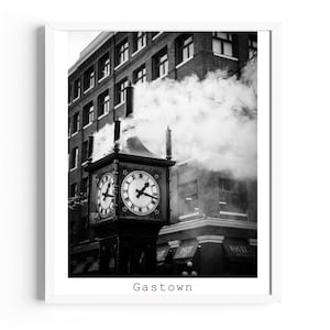 May include: Black and white photograph of a vintage clock tower in Gastown. The clock has four faces with Roman numerals. Steam rises from the top of the tower, with buildings in the background. The word "Gastown" is printed at the bottom.