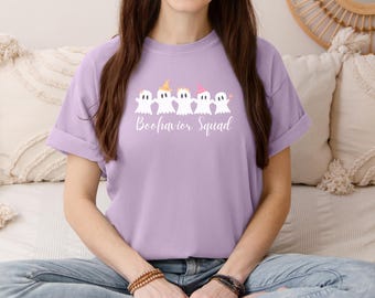 May include: A lavender t-shirt with a white graphic of five ghosts holding hands. The text "Boo-havior Squad" is printed below the ghosts.